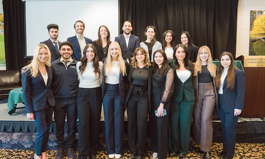 A group of law students in business attire are pictured smiling at the camera in a conference room