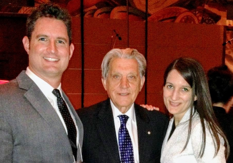 Two men and a woman in business attire smile at the camera