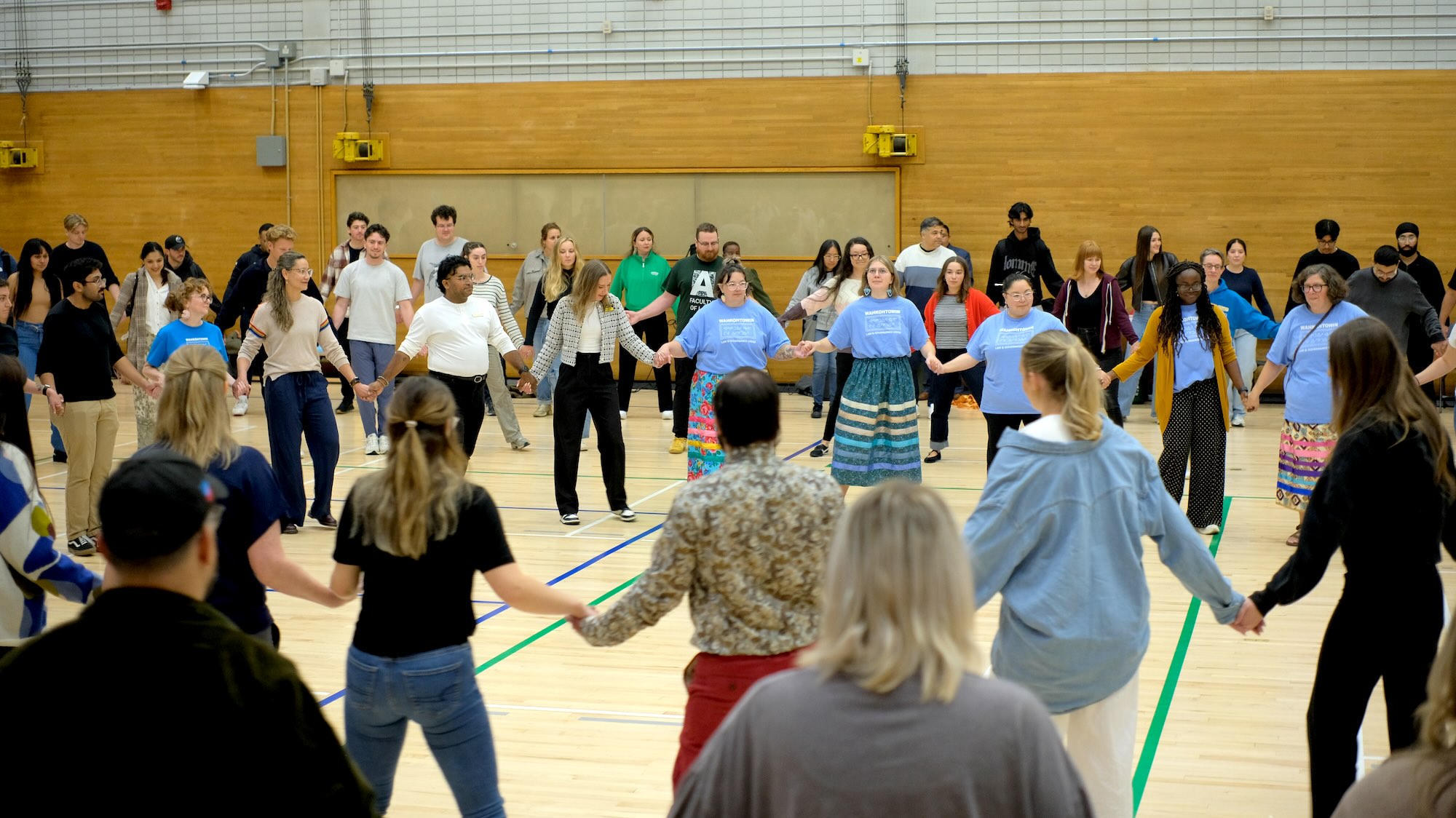 Law students participate in a circle activity led by two women in ribbon skirts, holding hands