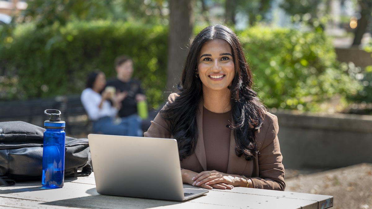 Law student at a picnic table on North Campus Quad smiling with her laptop and water bottle
