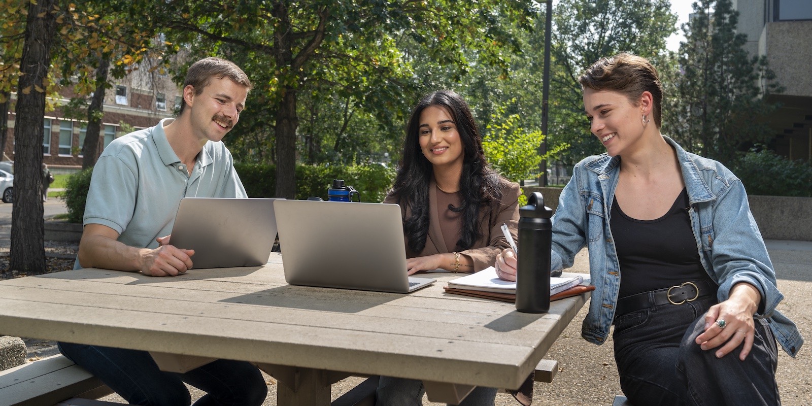 Three students studying outside at a picnic table in Quad