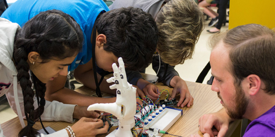 Three children work with mechanical hand controls under the supervision of a DiscoverE camp leader
