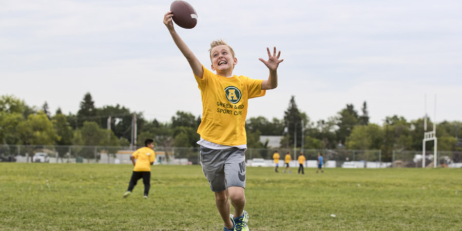 A child reaches to catch a football outside during a Green and Gold sport camp