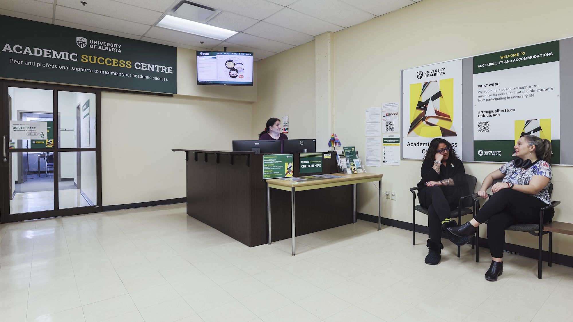 Two people talking while waiting in the lobby of the Academic Success Centre, with the receptionist behind the desk