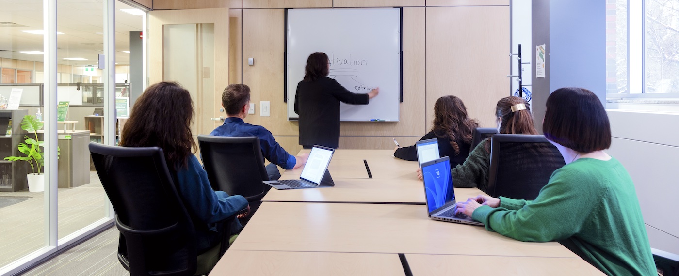 Woman leading a seminar in an Academic Success Centre boardroom with five people taking notes