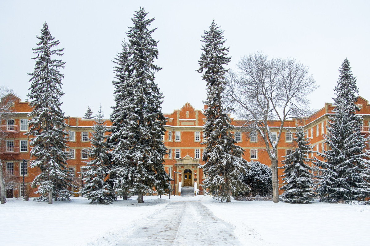 Athabasca Hall in winter, with a layer of snow covering the building, trees and quad.
